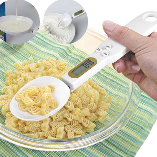 Hand holding digital kitchen scale with spoon measuring pasta over a glass bowl on a striped cloth